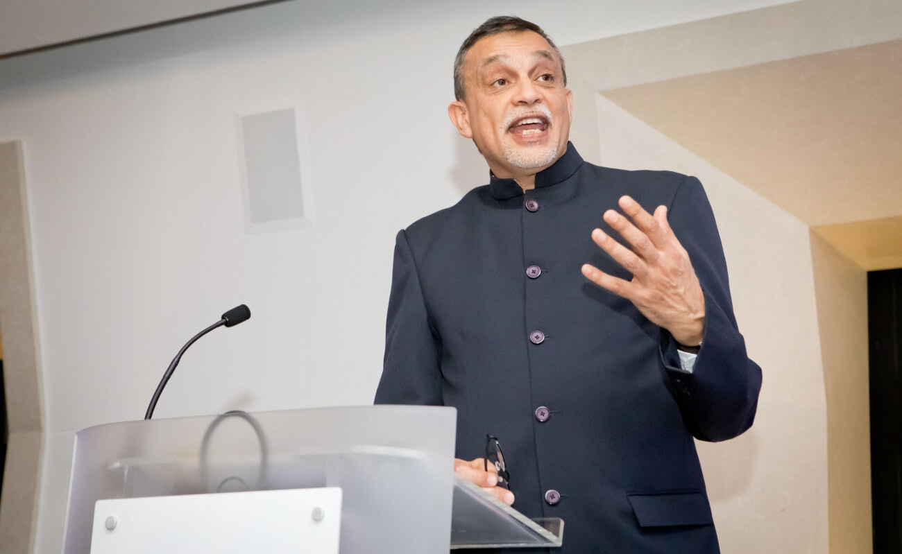 An image of Dr Aneez Esmail speaking at a lectern wearing a navy blue shirt.