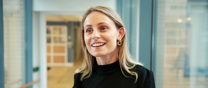 A young woman with blonde hair smiles at something or someone in the distance.