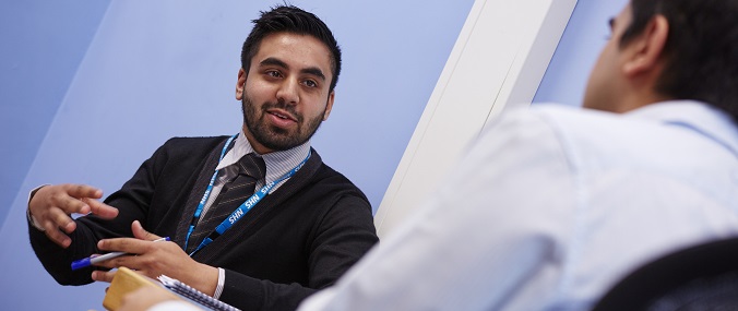 A doctor smiling and gesturing while in conversation with another doctor