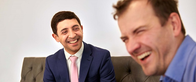 An image of two seated laughing men wearing suits.