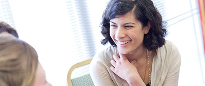 A woman with dark hair crosses her arms while laughing with others out of shot. 