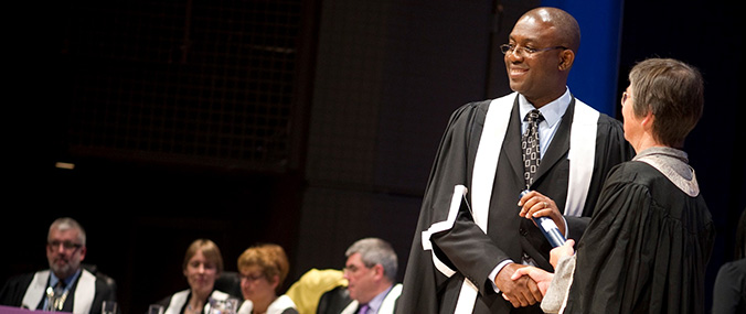 A woman shakes the hand of a male graduate as he accepts his certificate.