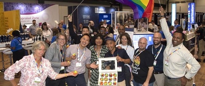 A group of people standing in a large room posing with cupcakes and rainbow flags.