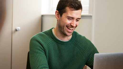 A man wearing a green jumper enjoys a website on a laptop. 