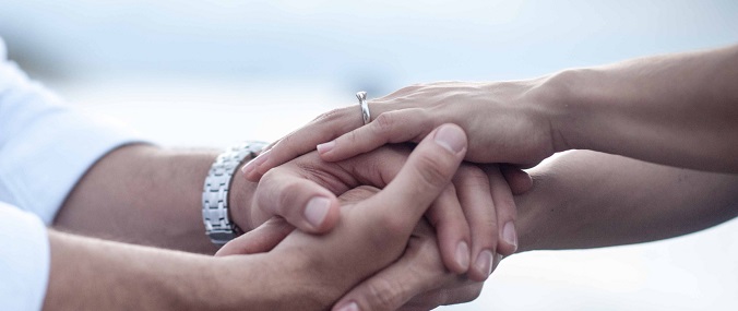Two people with wedding rings clasping each other's hands