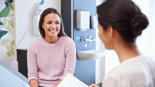 A photo of young woman visiting a GP wearing white in her practice office. 