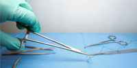 A gloved hand grips a metal surgical tool next to a table with a blue cloth. 