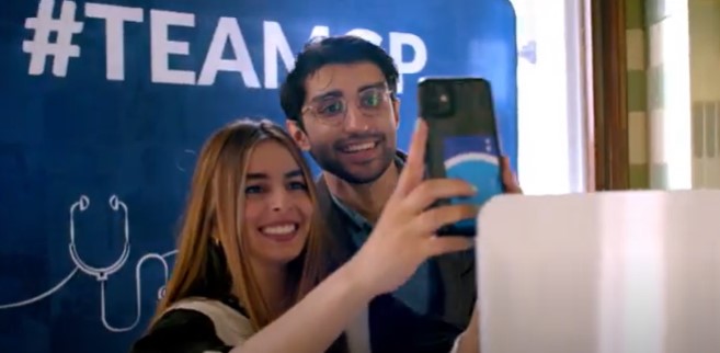 Two smiling people taking a selfie in front of a backdrop reading #TeamGP