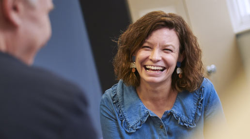 A woman wearing a denim shirt laughs with a friend out of shot.