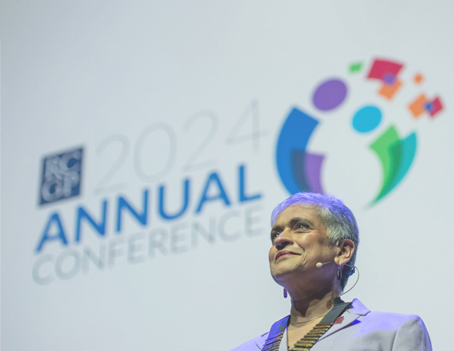 RCGP Chair Professor Kamila Hawthorne stands in front of a large white screen with the RCGP logo in the center. 